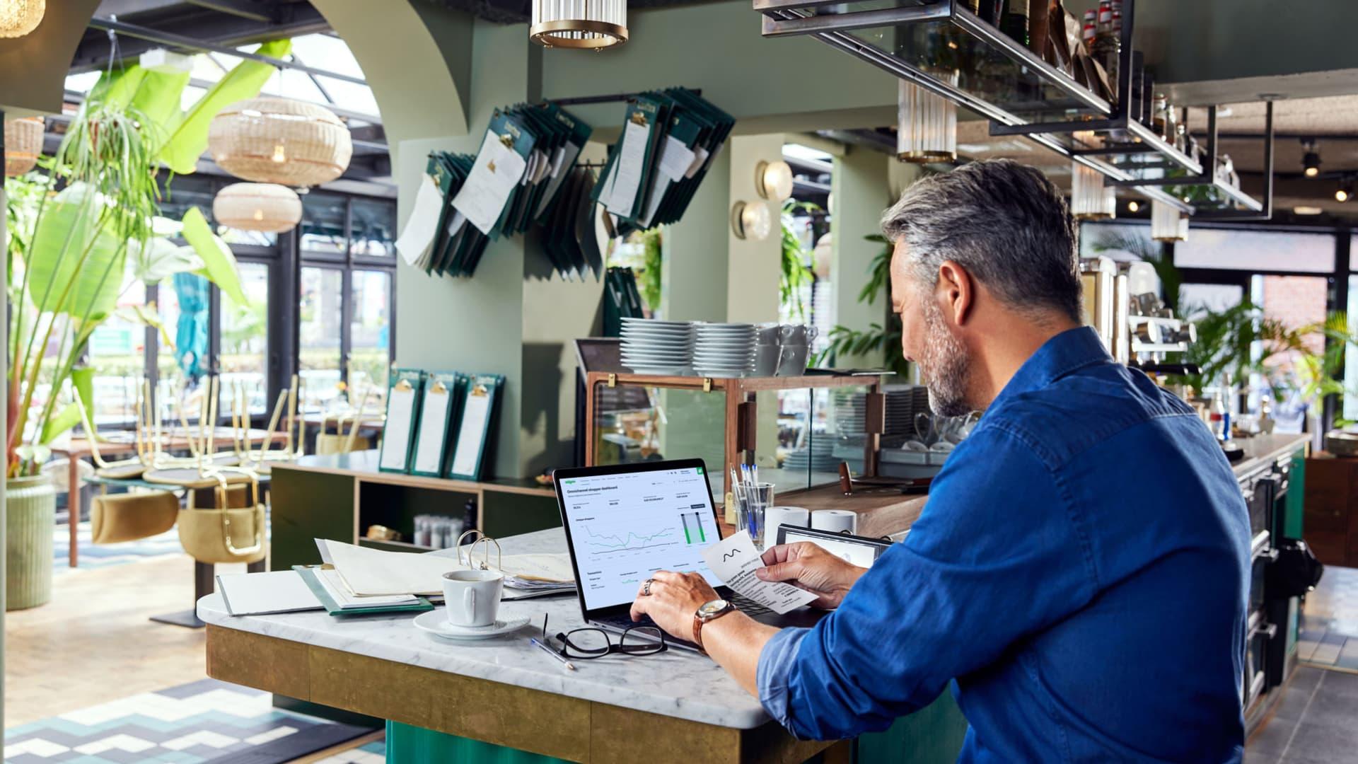 Un homme d'affaires analyse les analyses Adyen sur un ordinateur portable dans un café.