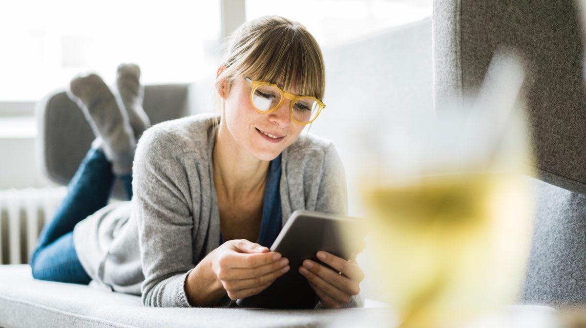 Mulher de óculos deitada no sofá usando um tablet