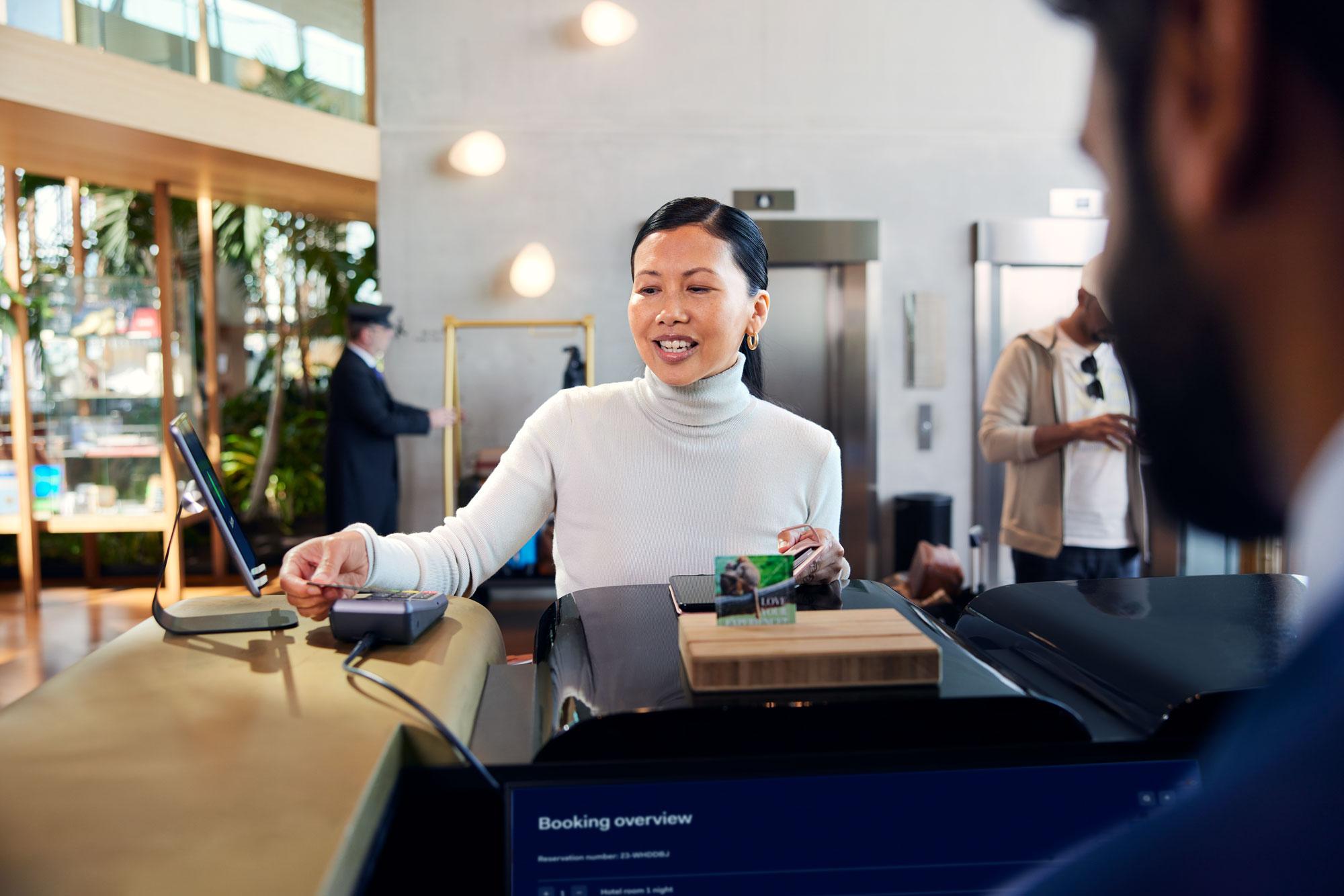 En kvinne ved resepsjonen på et hotell som gjør et betaling ved å tappe et kort på Adyens P400 Plus-terminal.