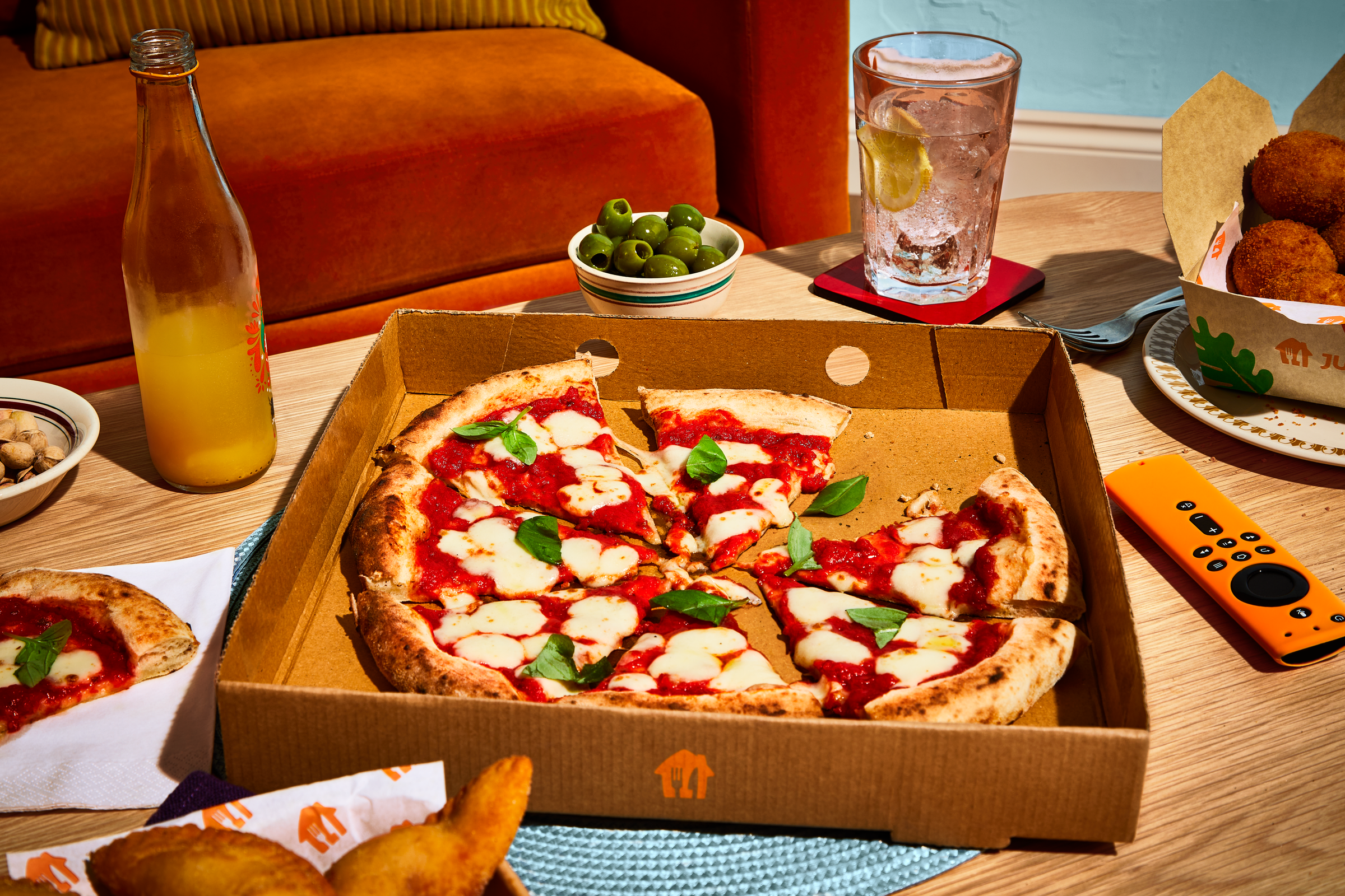 Pizza with cheese and basil on a table with drinks around it. 