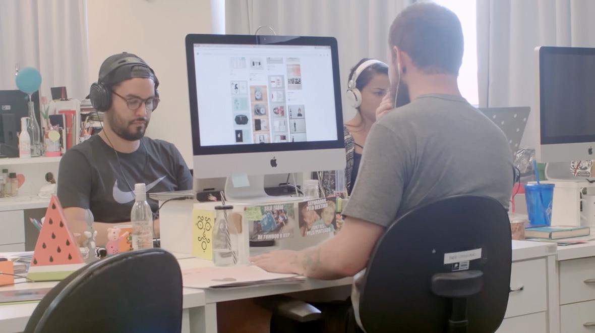 Duas pessoas trabalhando em mesas com computadores em um ambiente de escritório moderno.