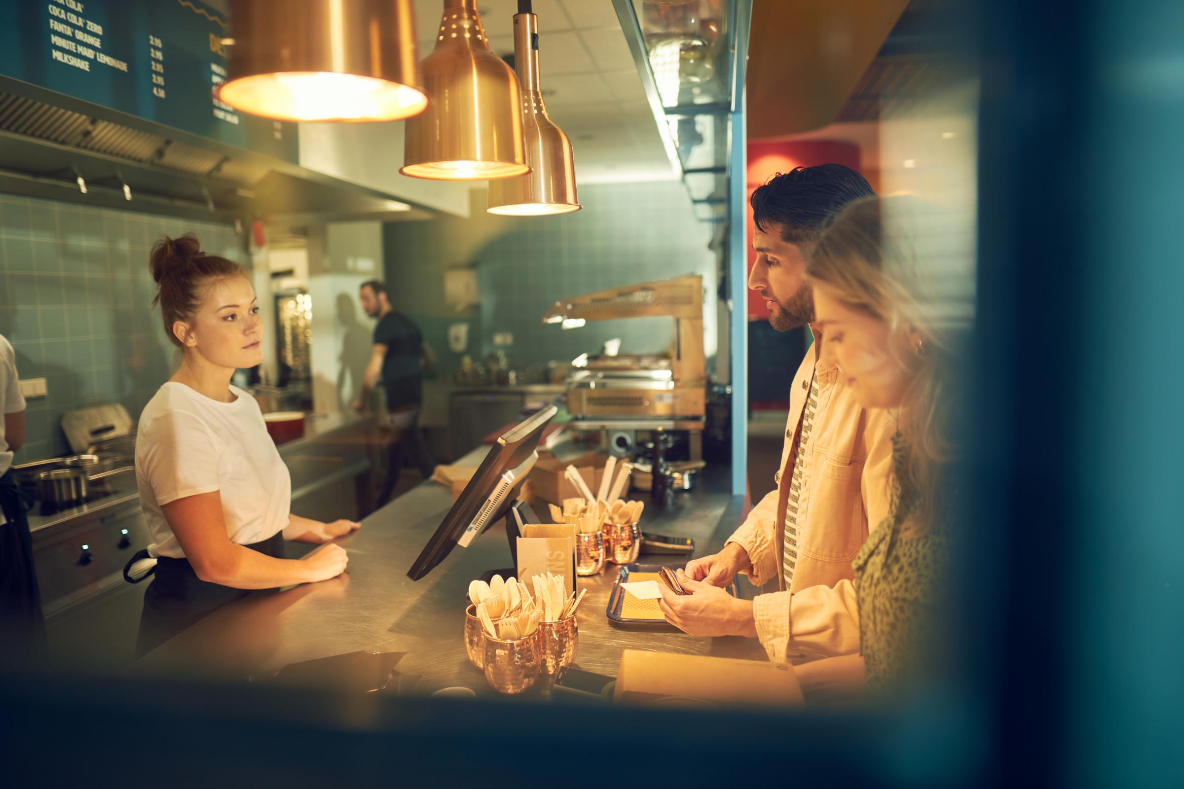 Kunder som gör ett betalning vid en restaurangdisk med en anställd som närvarar