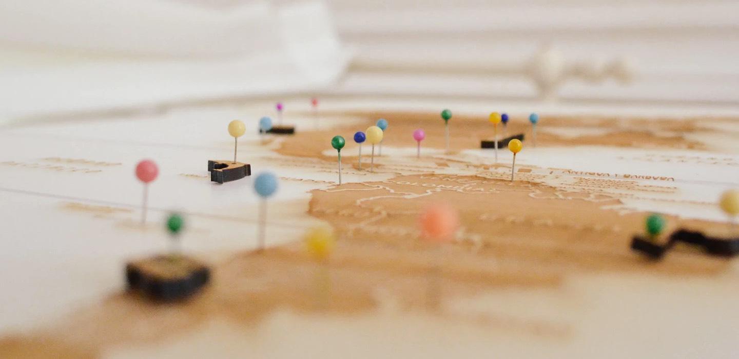 Close-up of a wooden map with colorful pins marking different locations.