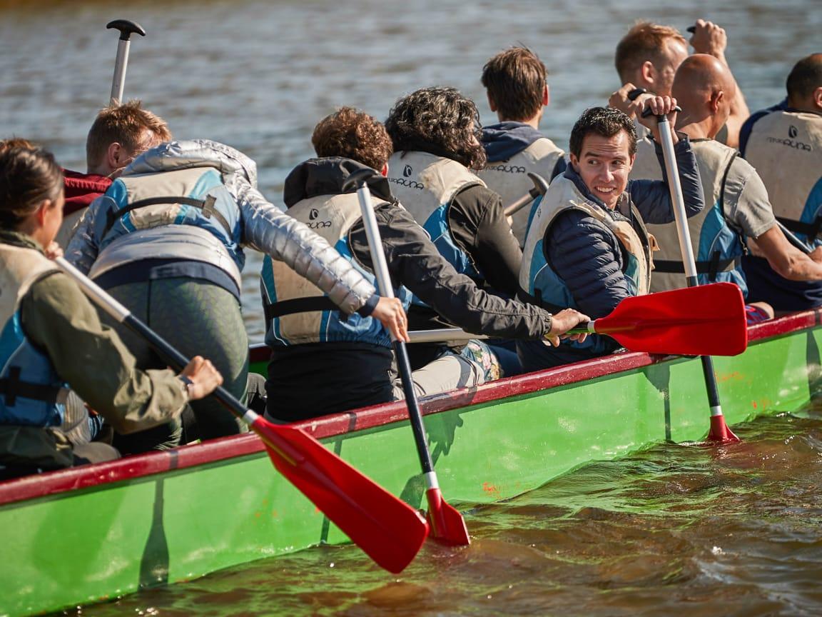 Team of people paddling in a green dragon boat on water.