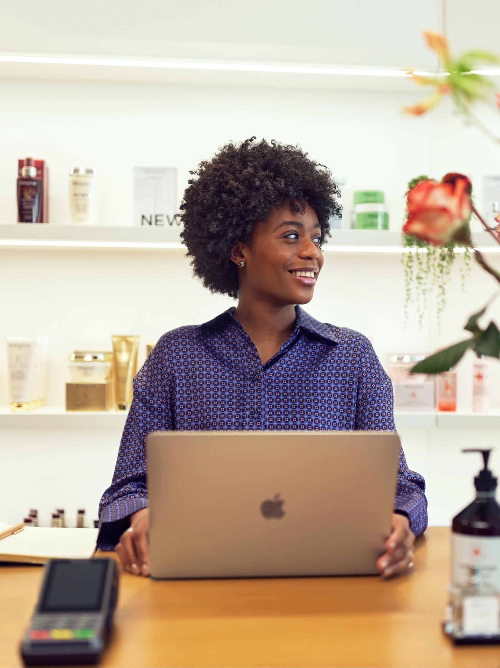 Donna sorridente al bancone di vendita con laptop e terminale di pagamento Adyen