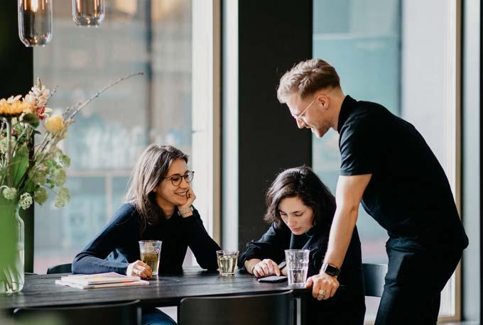 A waiter attending to two customers sitting at a cafe table.