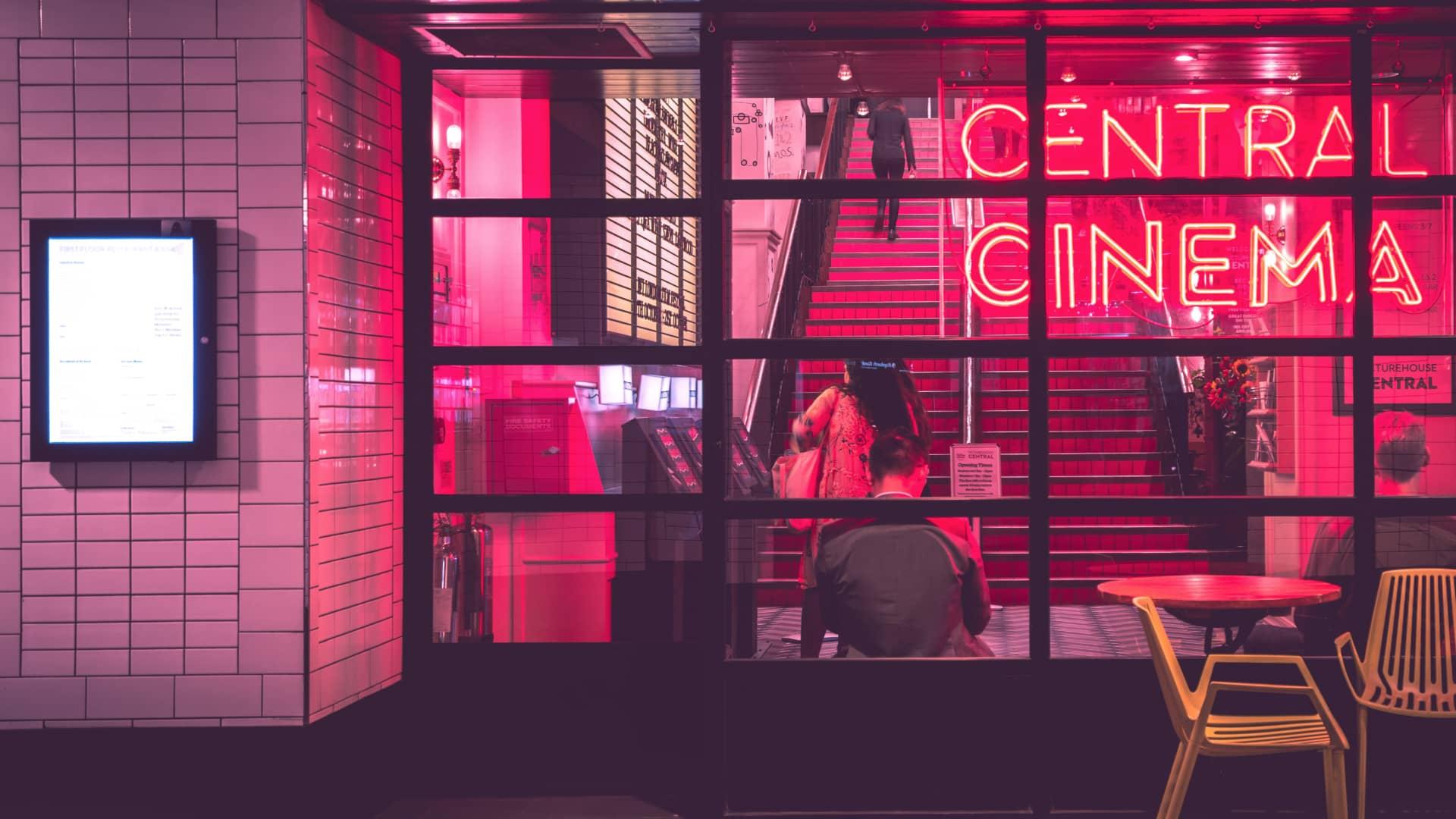 Letreiro de neon com 'CENTRAL CINEMA' acima da entrada do cinema com clientes