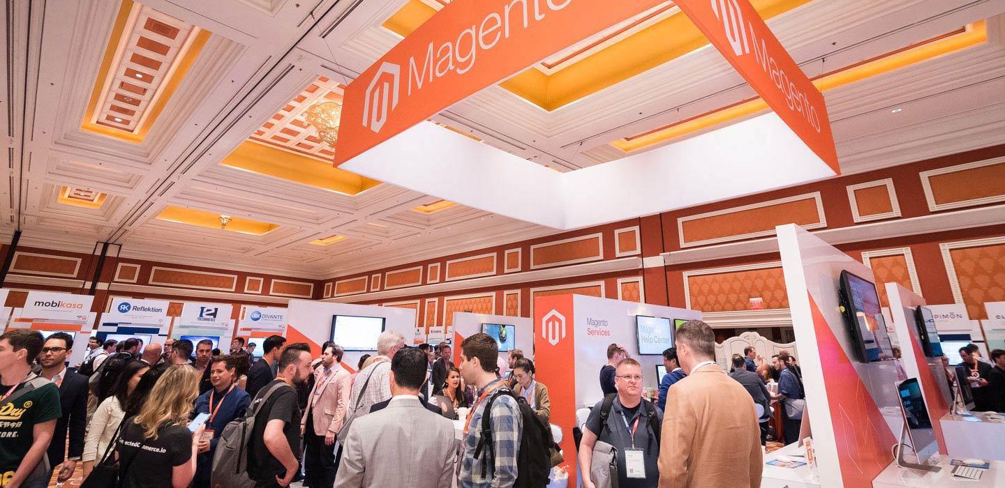 Participantes em networking em uma conferência Magento com estandes e banners