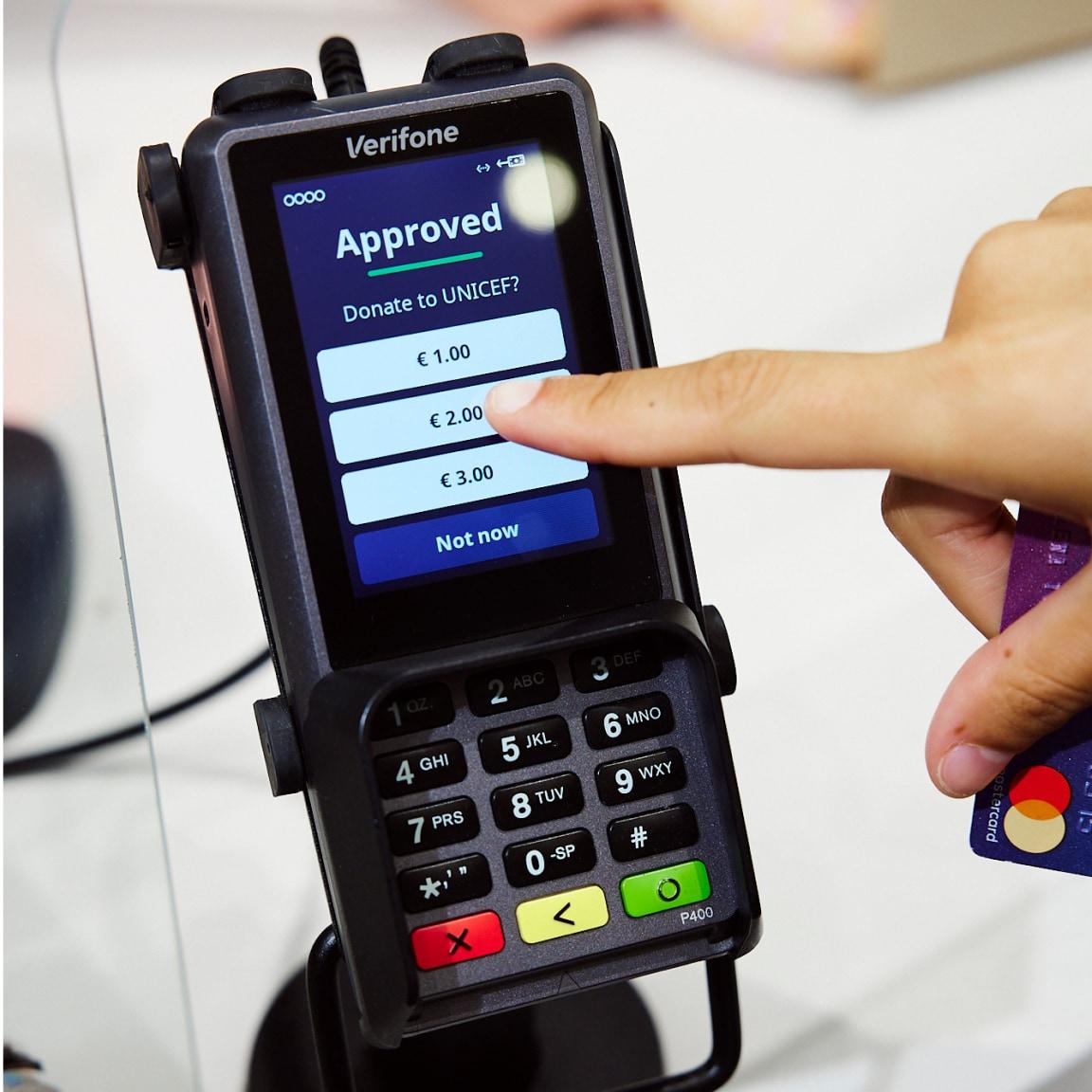 Finger selecting donation options on a payment terminal screen displaying 'Approved' and Adyen logo.