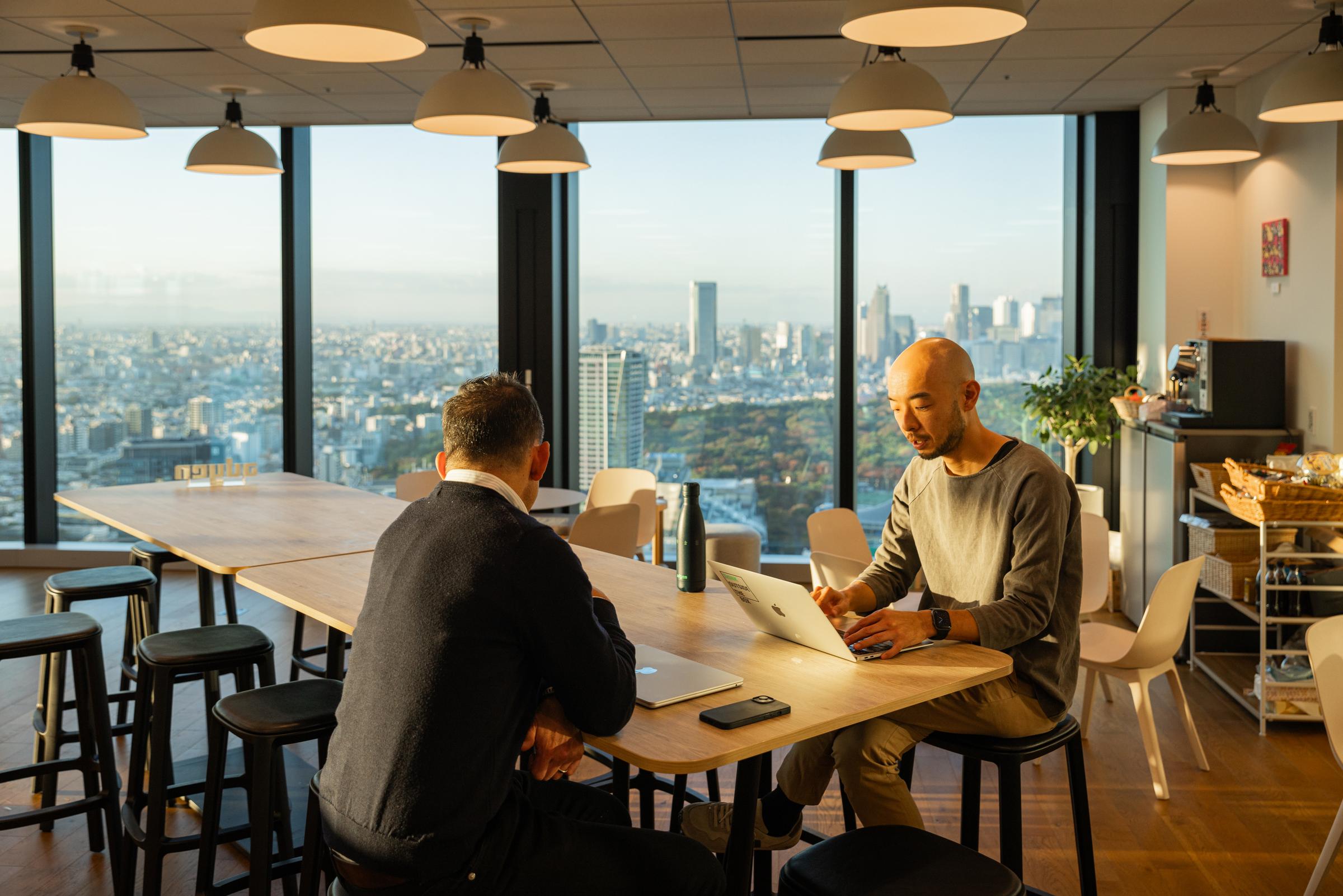 Two colleagues sitting in the office at a table behind their laptops 