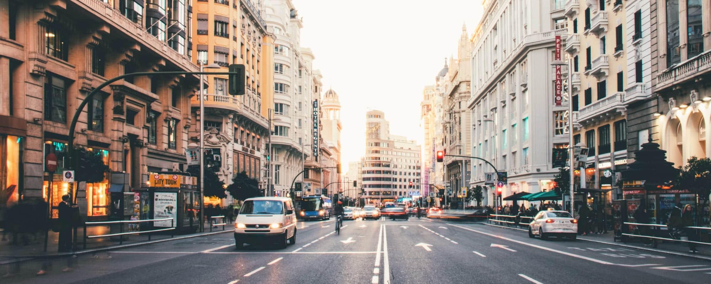 Sunlit city street with cars, buses, and classic architecture during evening rush hour.