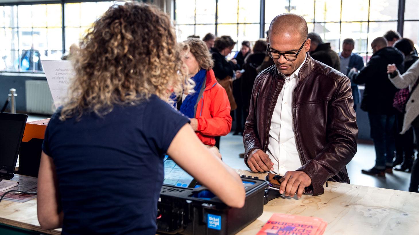 Person using Adyen payment terminal at a busy event registration desk.