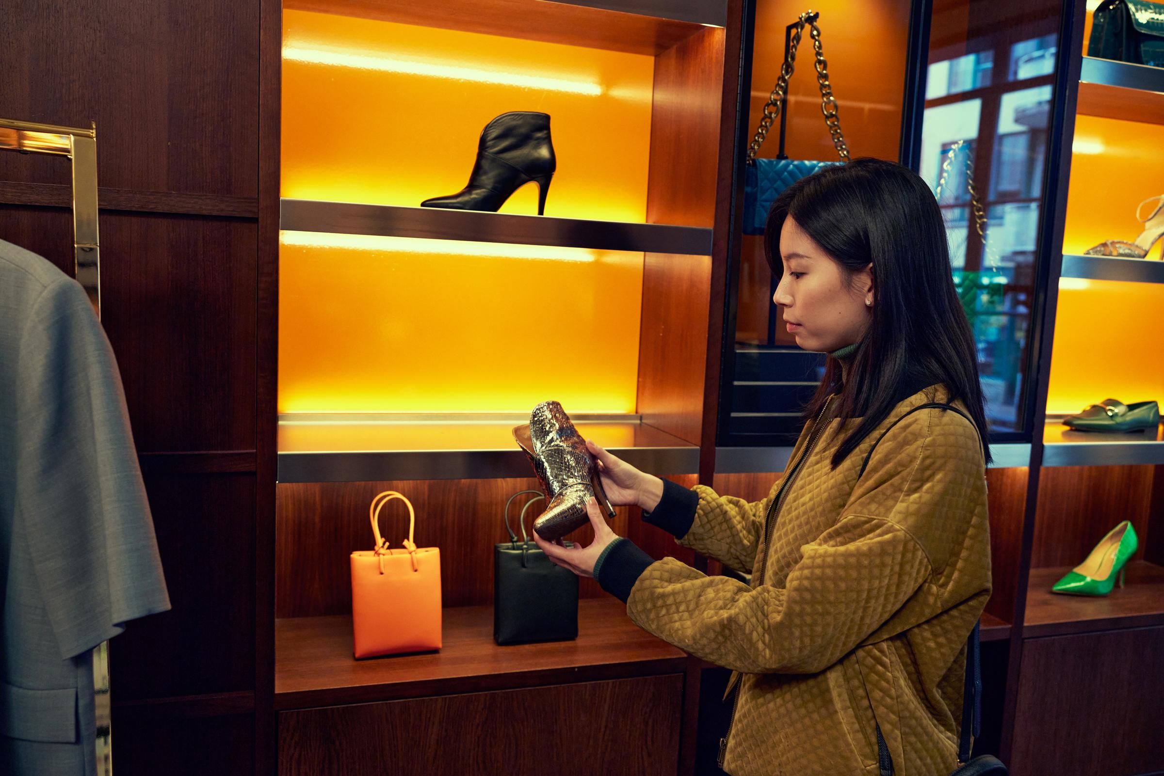 Women holding a shiny silver high heel shoe in a luxury clothing store.