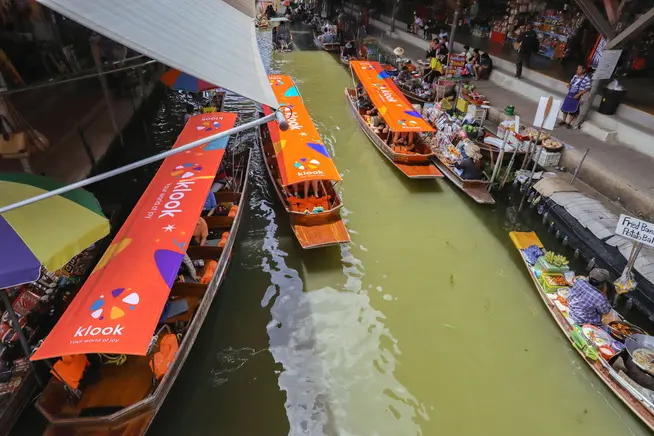 A floating market in Thailand with three Klook boats moving between the shops.