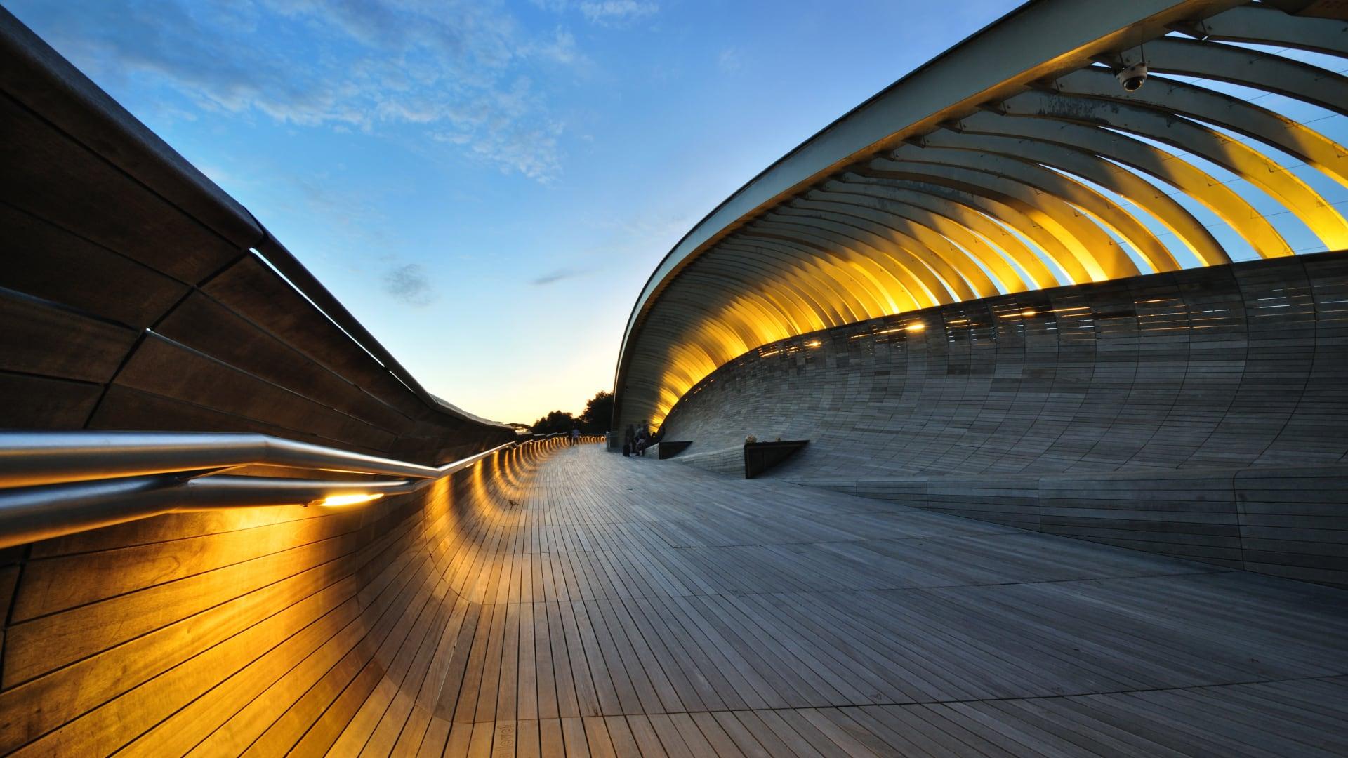 Curved modern structure with illuminated arches and wooden deck at dusk in Singapore.