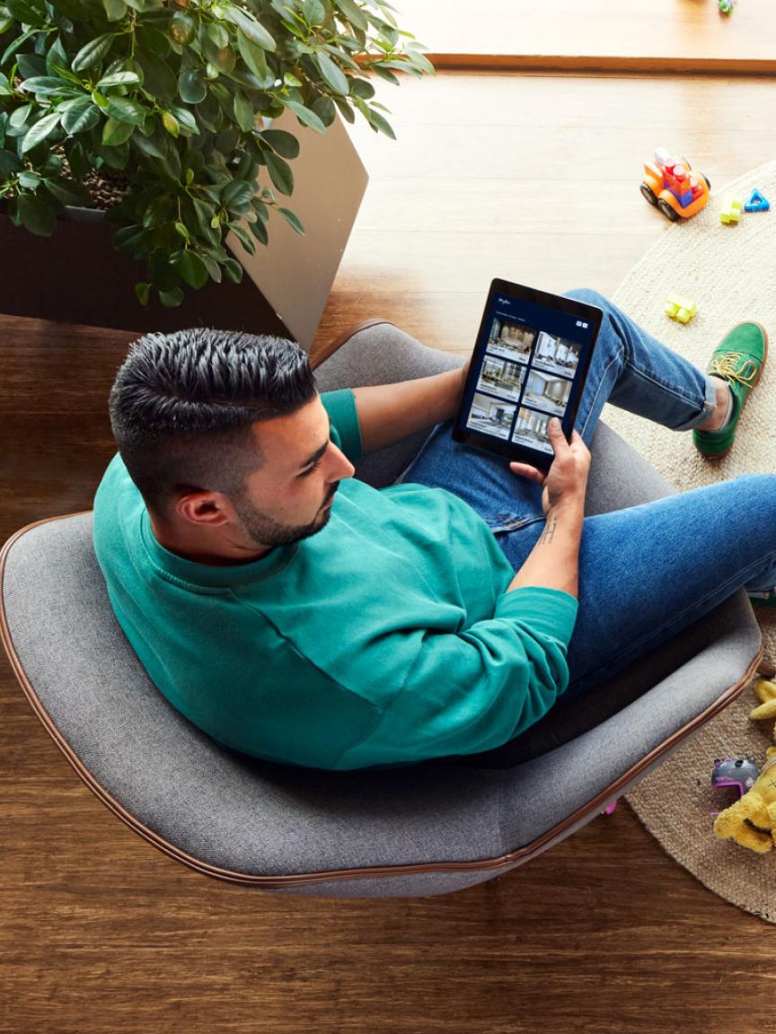 Homme assis sur une chaise en utilisant une tablette à côté d'une plante et de jouets pour enfants.