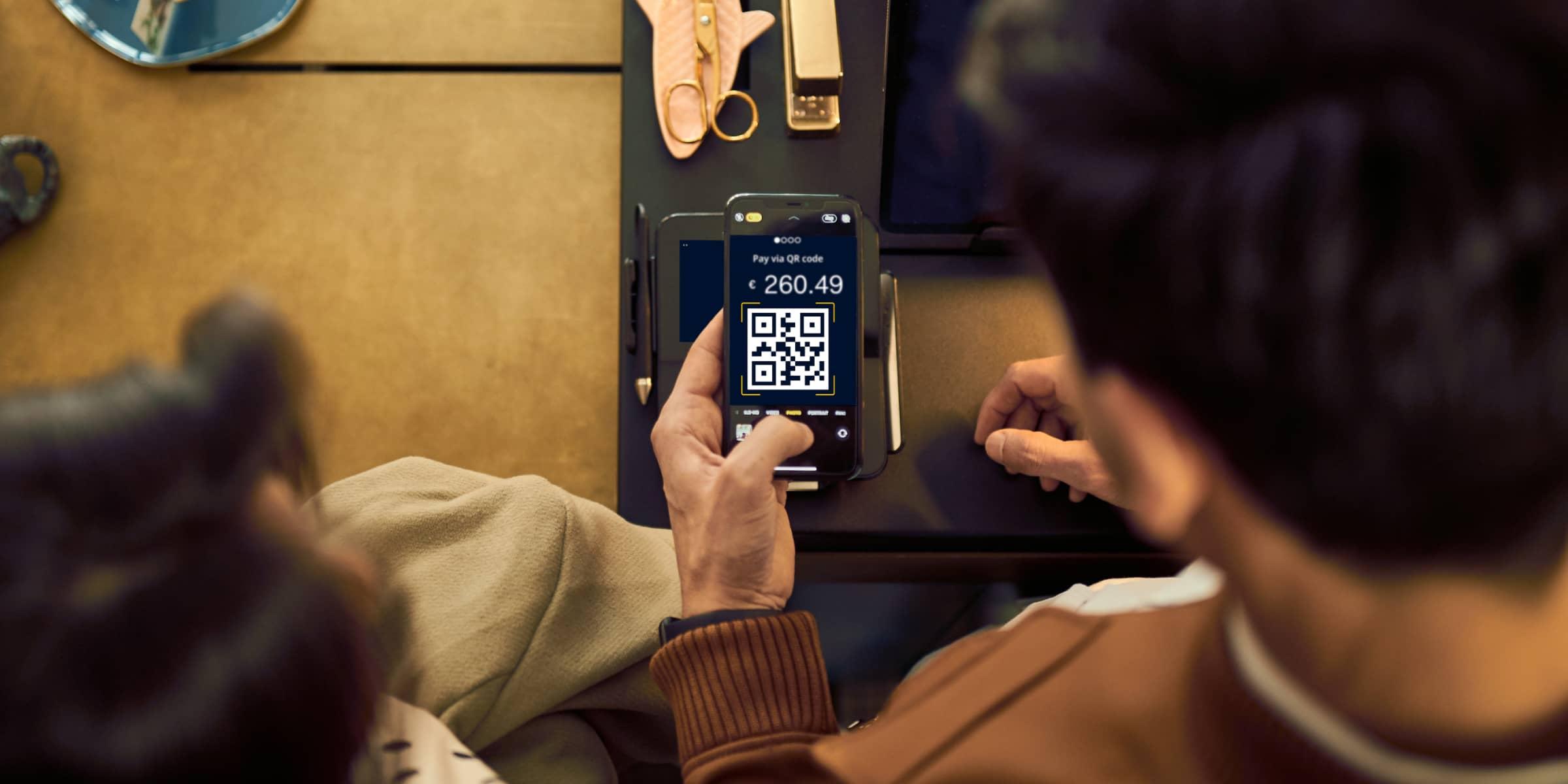 Two individuals processing a payment using an Adyen QR code on a mobile device.