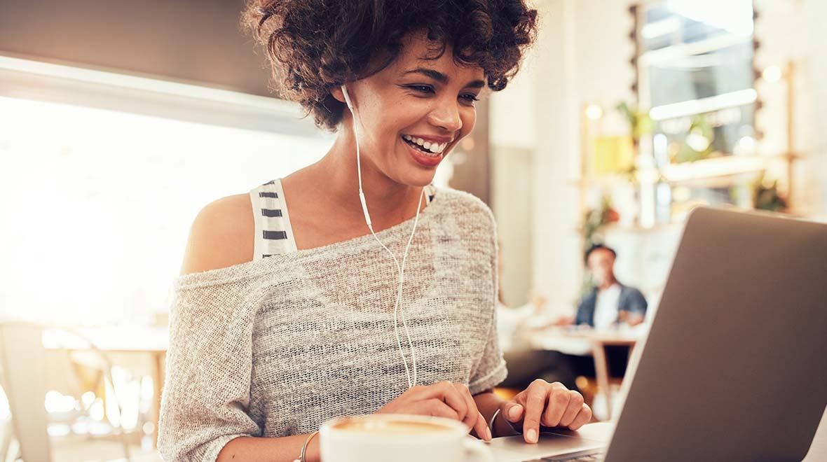 Mujer sonriendo con auriculares utilizando una laptop en un café.