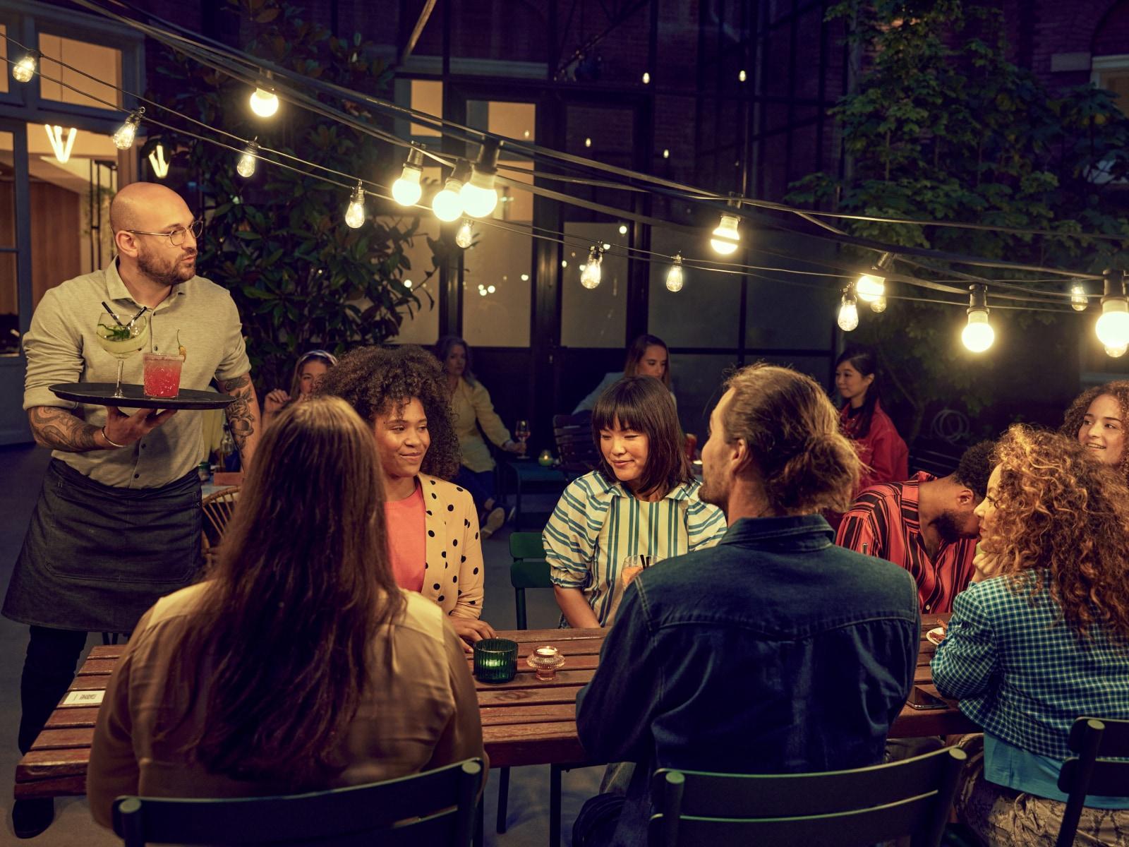 Číšník servírující koktejl hostům na útulném večerním venkovním setkání