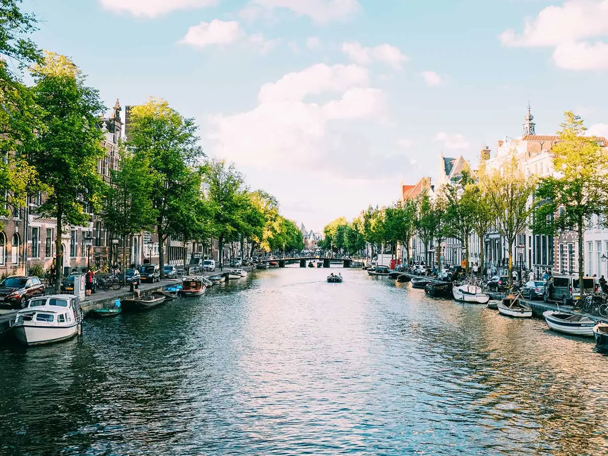 Sunny day view of boats on a tree-lined canal with historic buildings on either side.