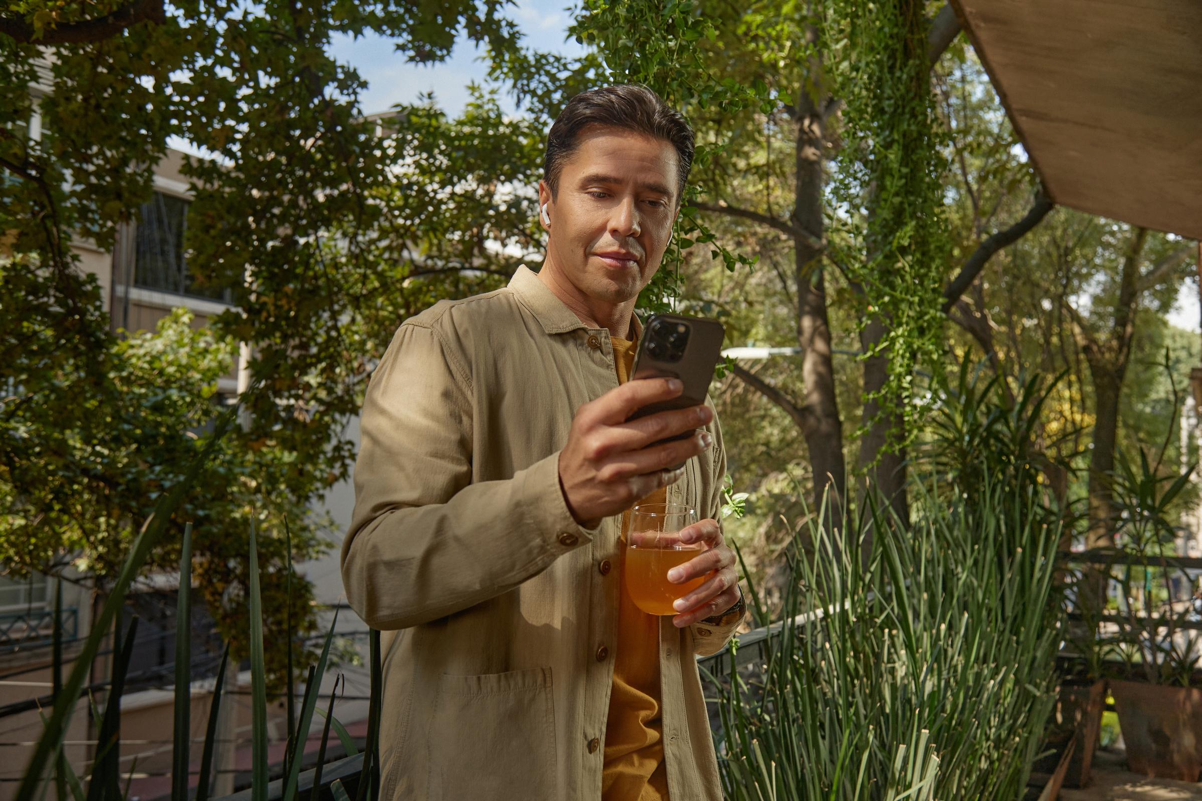 Hombre con ropa casual mirando el smartphone con auriculares en un entorno de jardín.