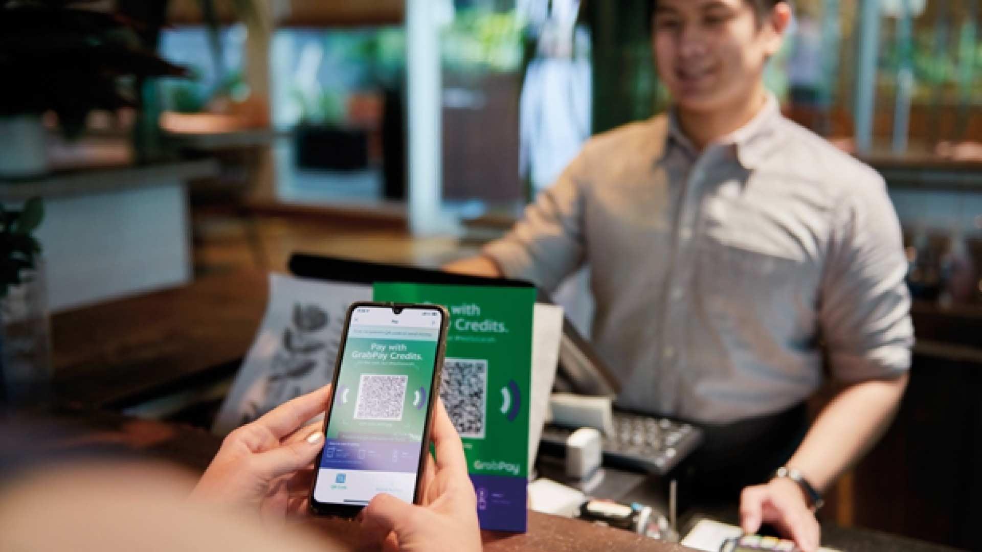 Customer making a mobile payment using QR code at a cafe with cashier smiling in the background.