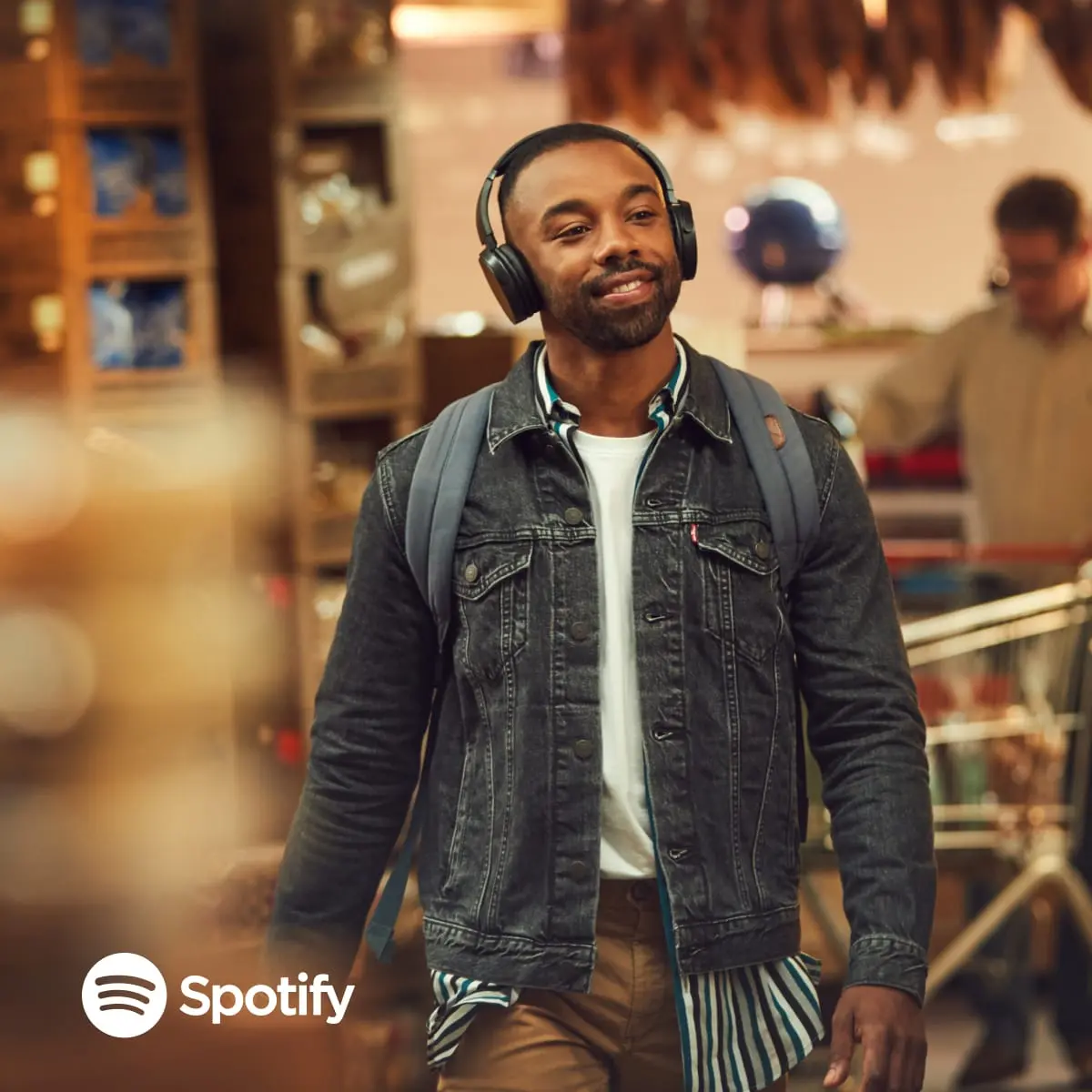 Man smiling while walking and listening to music with Spotify logo visible on his headphones.