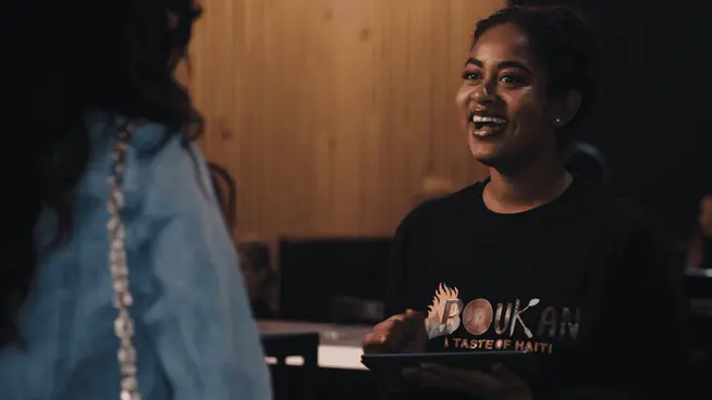 Smiling waitress wearing a Boukan shirt holding a digital tablet while taking an order.