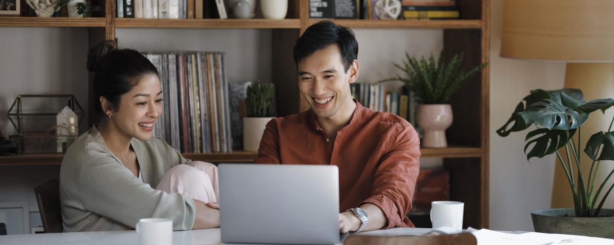 Two people smiling while looking at a laptop screen in a home office setting.