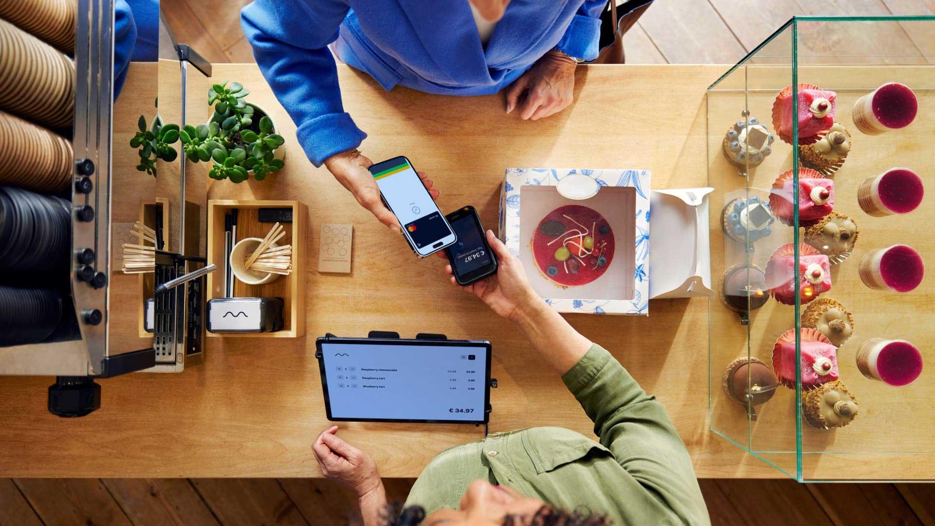 Customer making a wireless payment using a mobile device to a terminal next to a display of pastries.