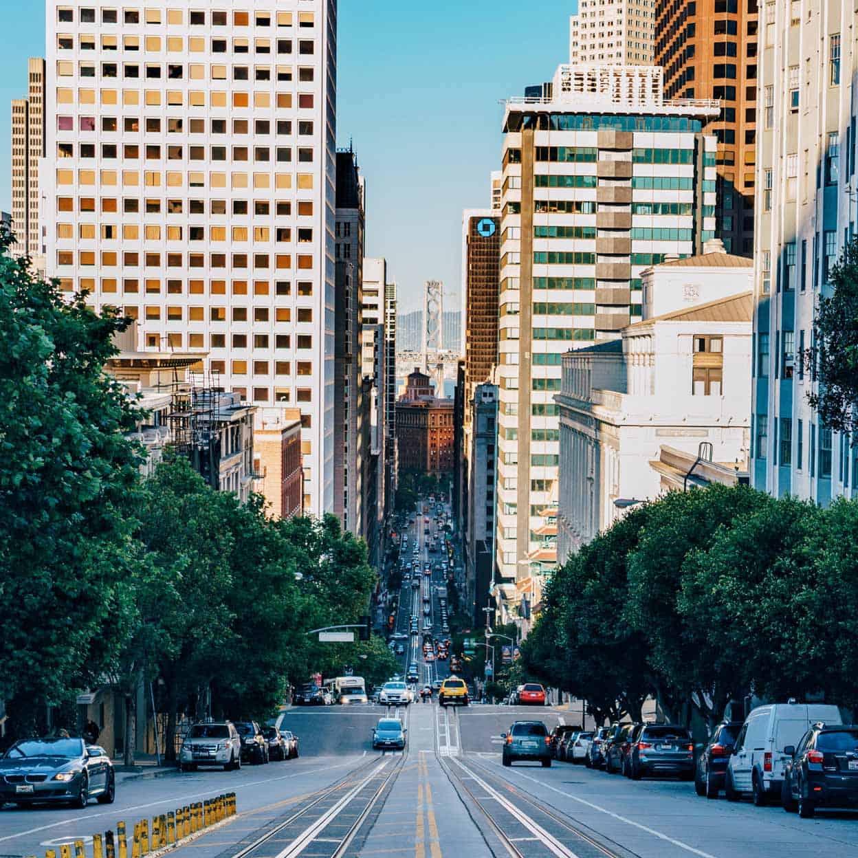 Steep city street with tram tracks lined by tall buildings and cars.