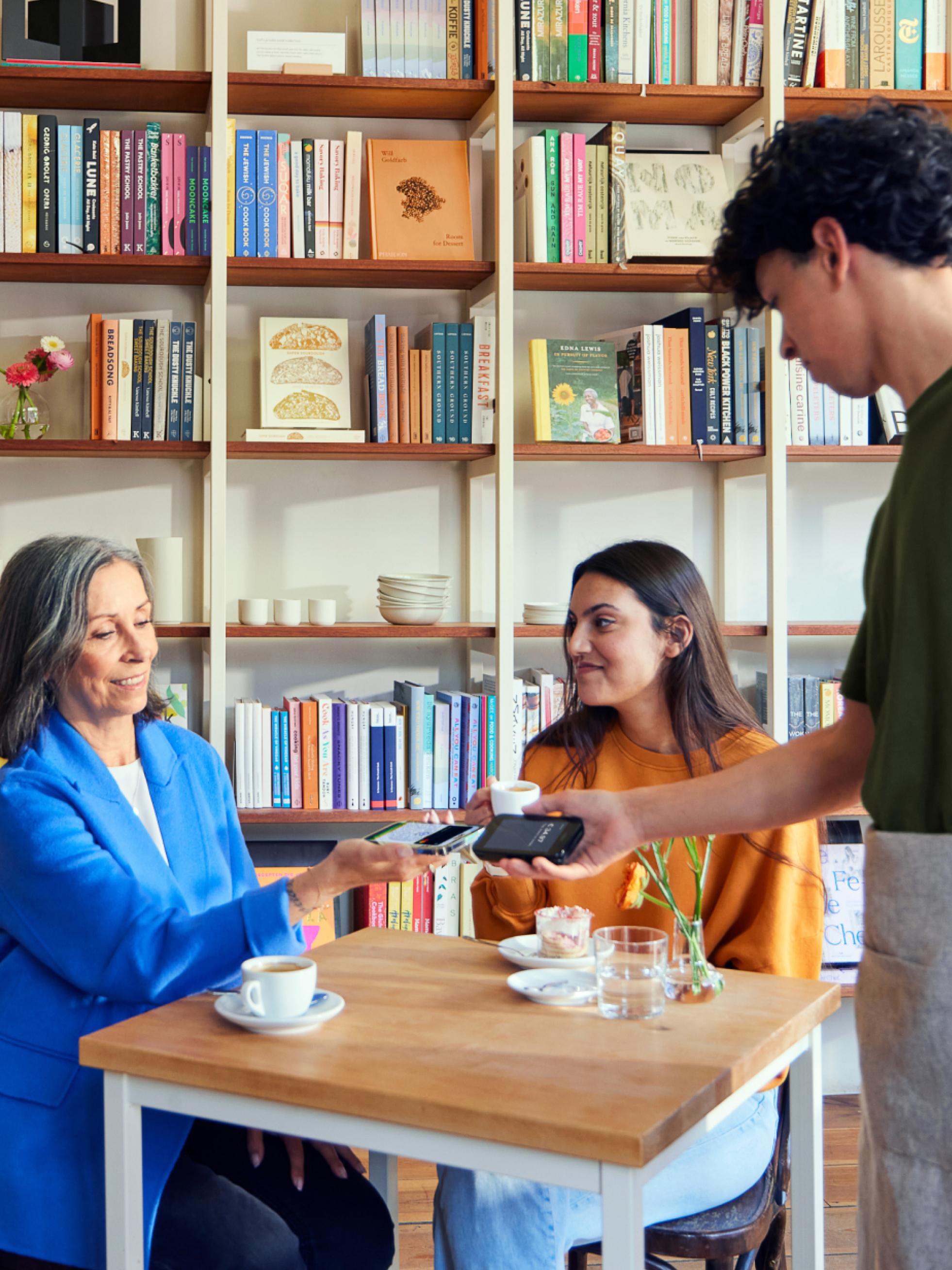 Due clienti seduti a un tavolo di caffetteria che effettuano un pagamento a un cameriere con un lettore di carte