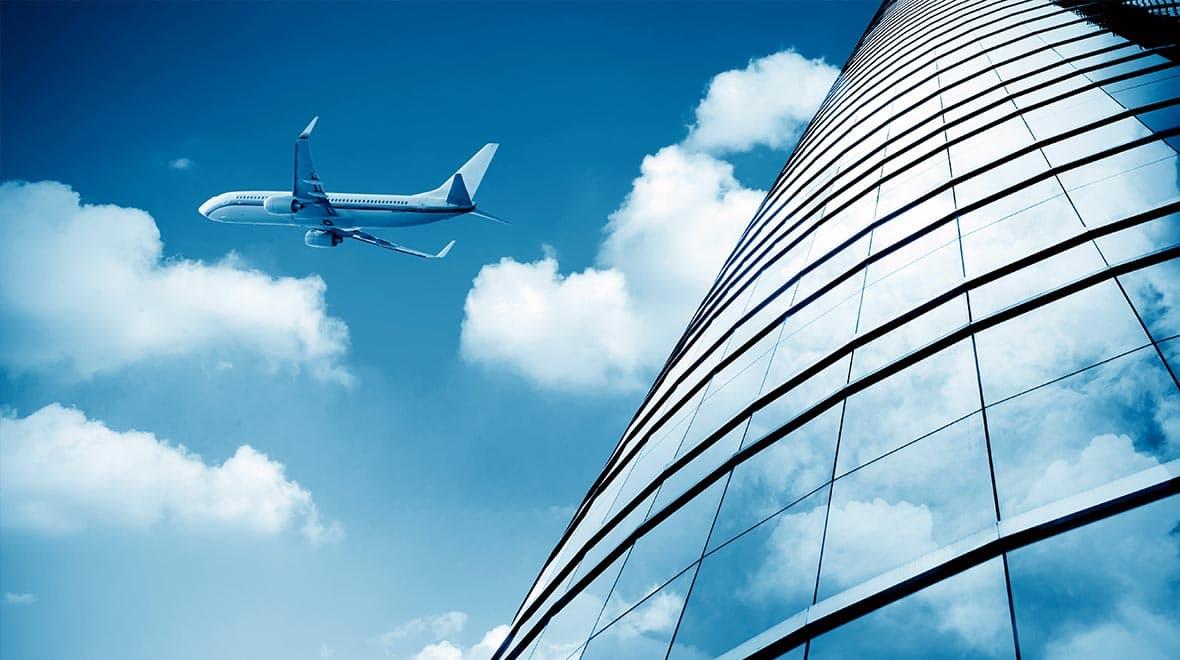 Avião voando sobre prédio de vidro moderno sob céu azul com nuvens.