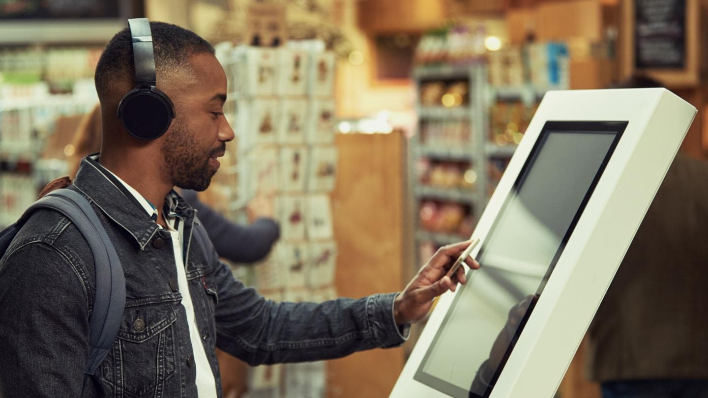 Homem usando um quiosque de tela sensível ao toque para interação digital em uma loja.