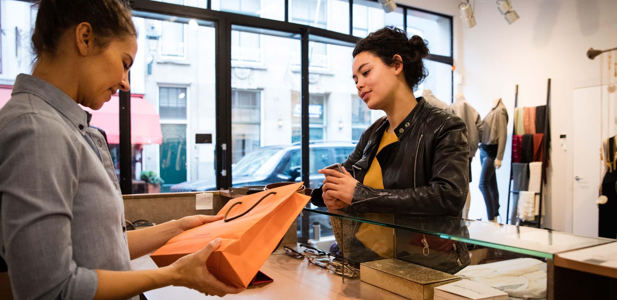 Cliente recebendo uma sacola de compras de um caixa em uma loja de boutique