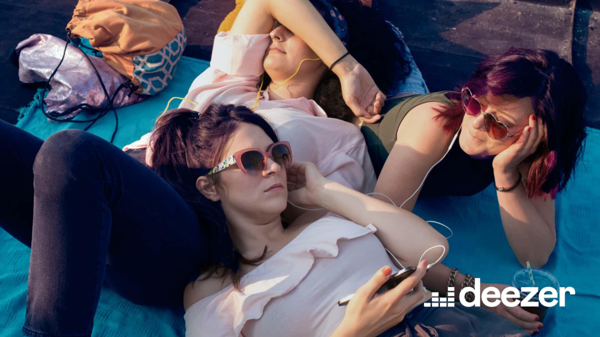 Trois personnes se détendent et écoutent de la musique à l'extérieur avec la marque Deezer.