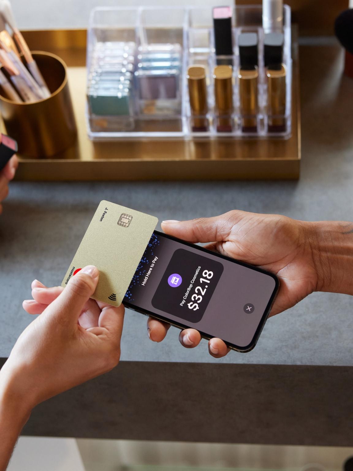 Primer plano de un pago sin contacto realizado con una tarjeta de oro y un smartphone que muestra el monto de la transacción.