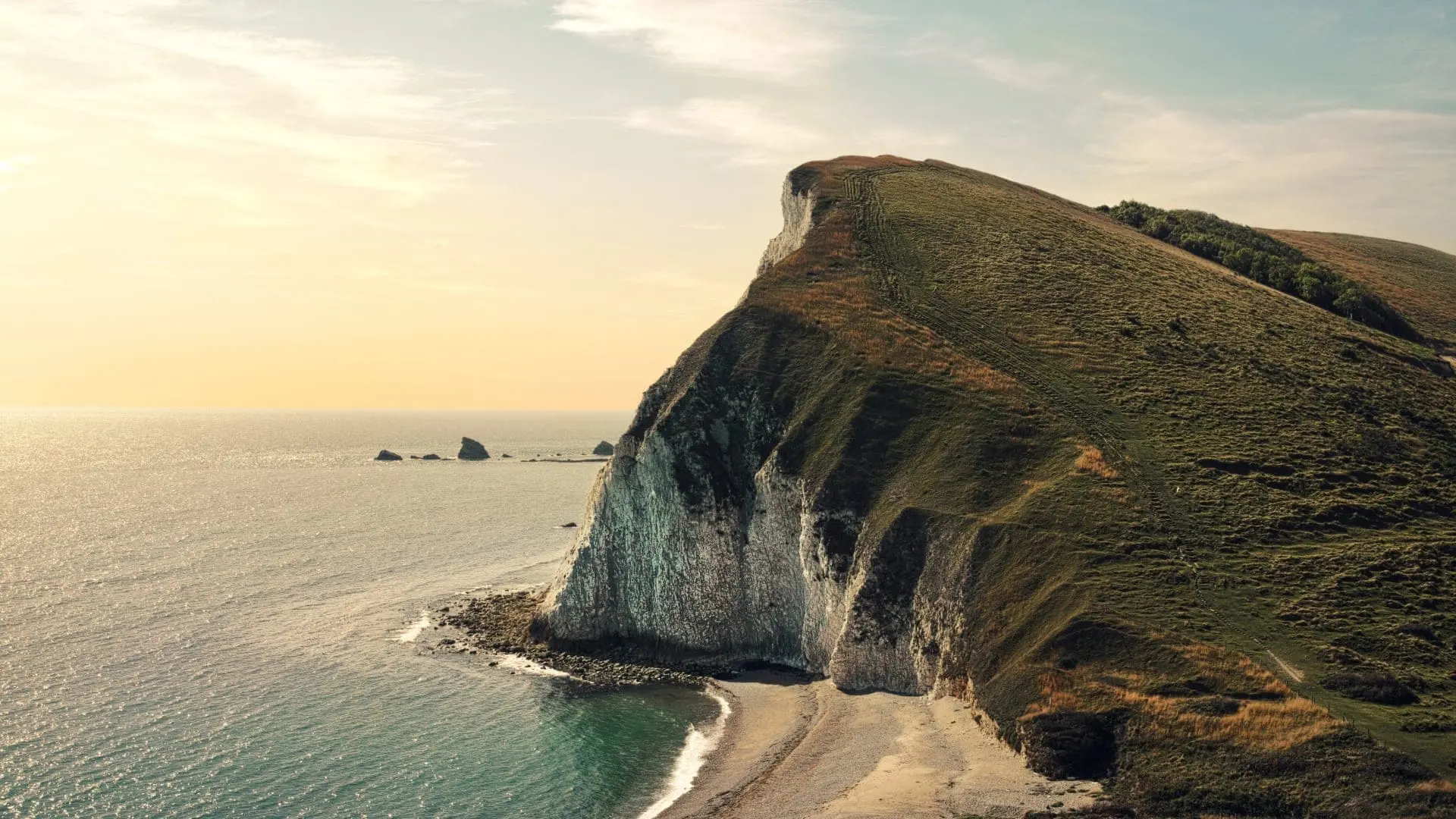 Coastal cliffs with a grassy hillside and a beach at sunset in the United Kingdom.