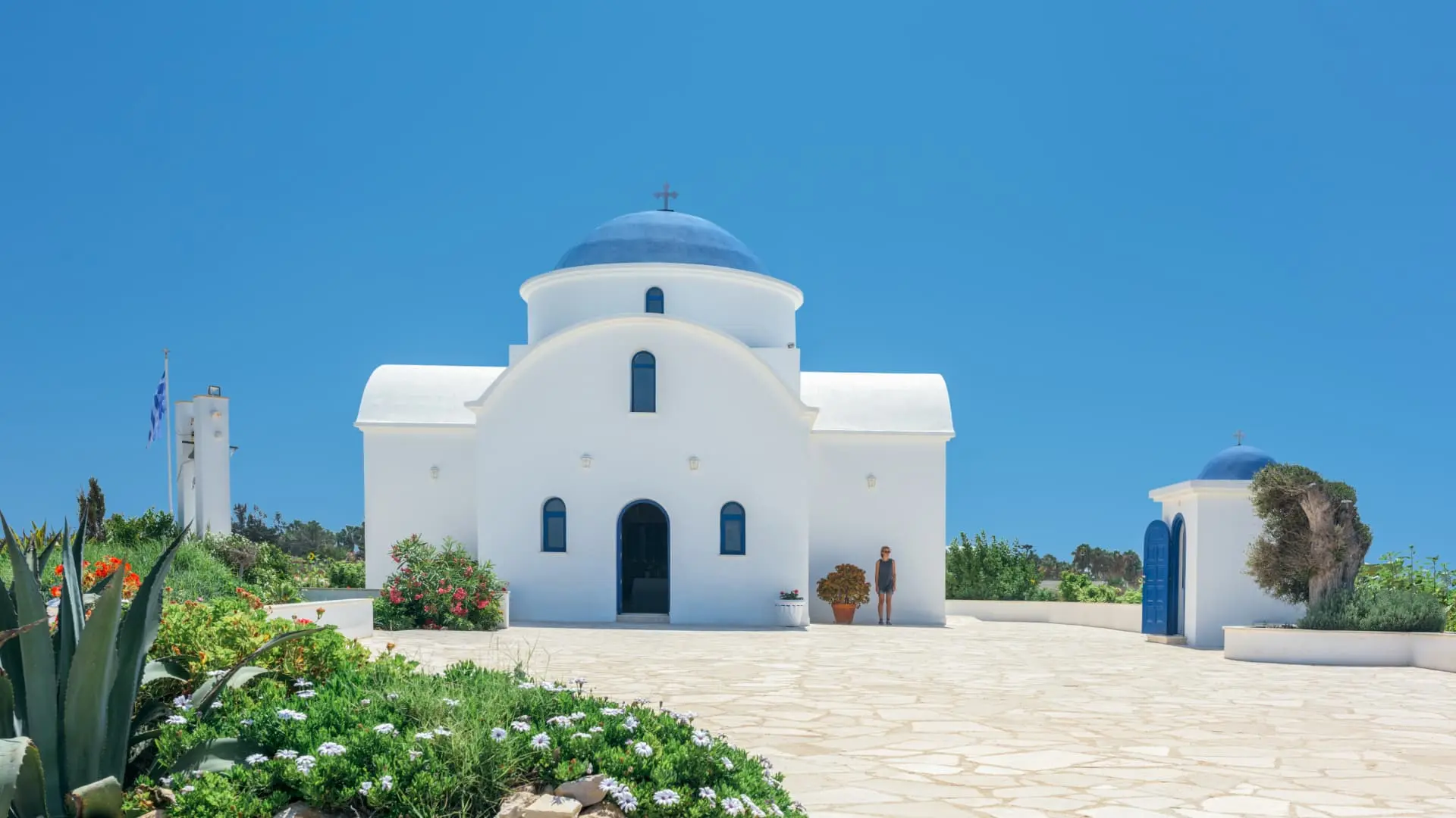 Traditional white church with blue dome and bright flowers under a clear blue sky in Cyprus.
