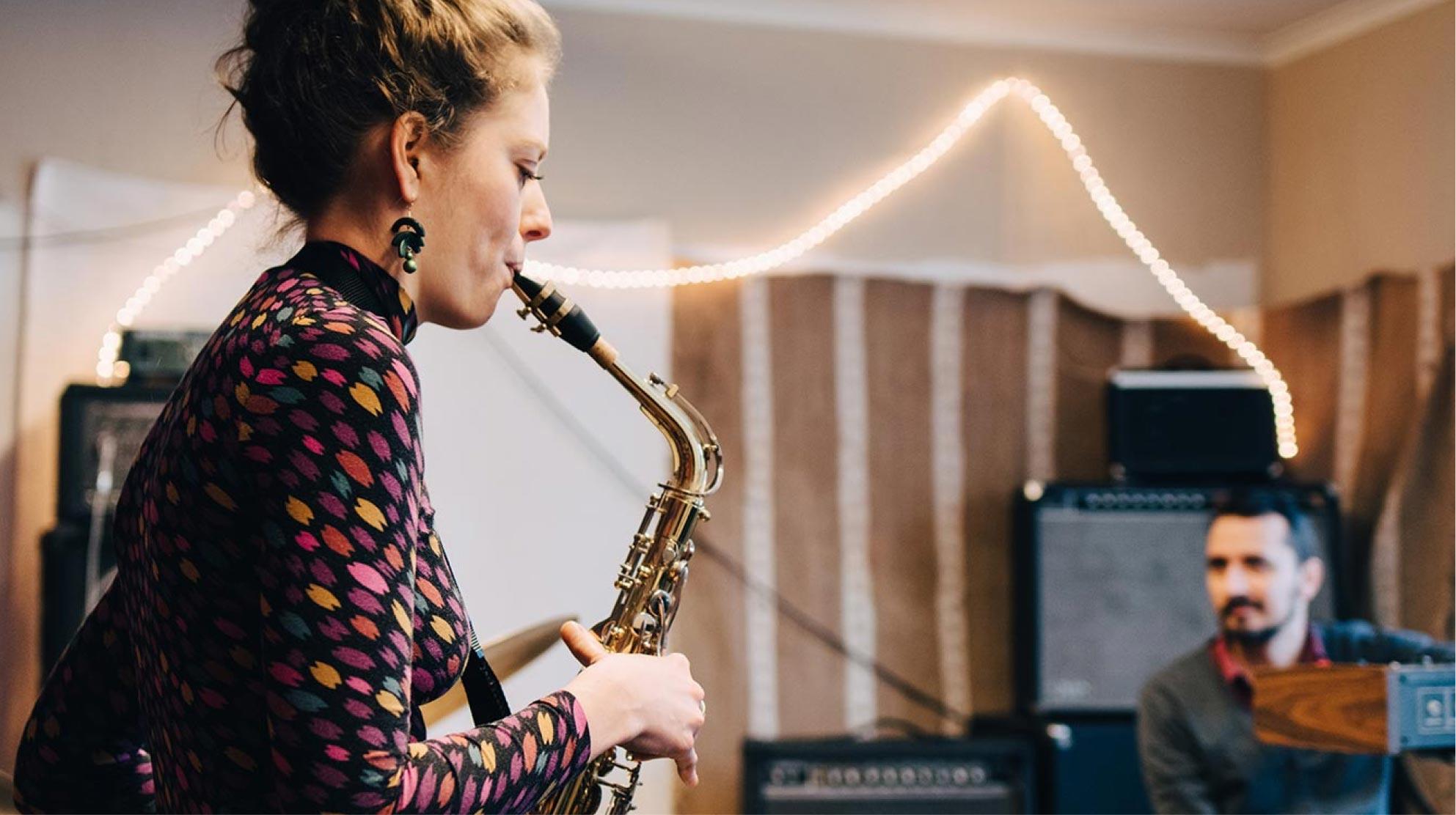 Frau spielt Saxofon mit einem Mann im Hintergrund