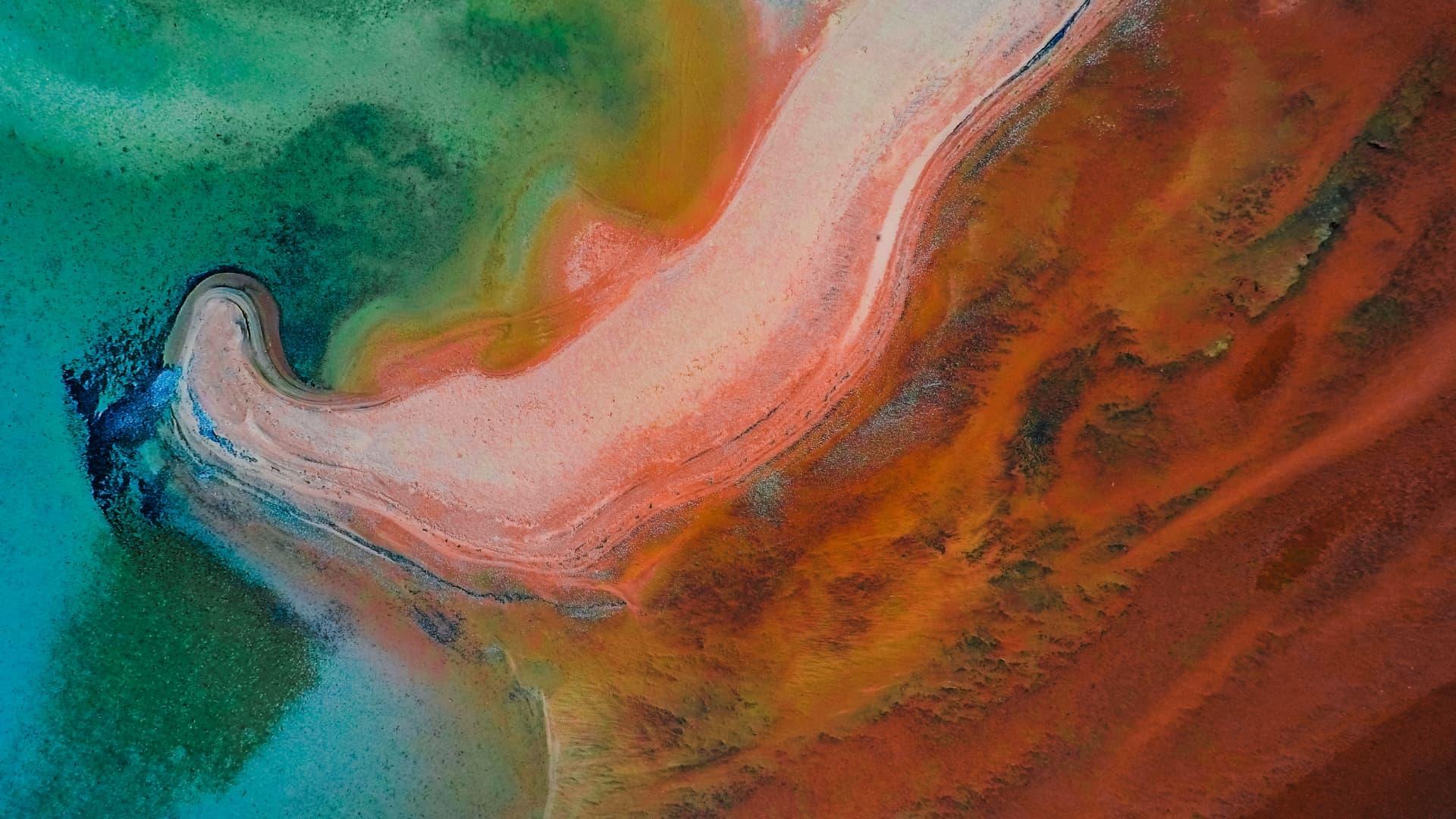 Aerial view of a colorful, abstract landscape resembling flowing water and beach sand in Australia.