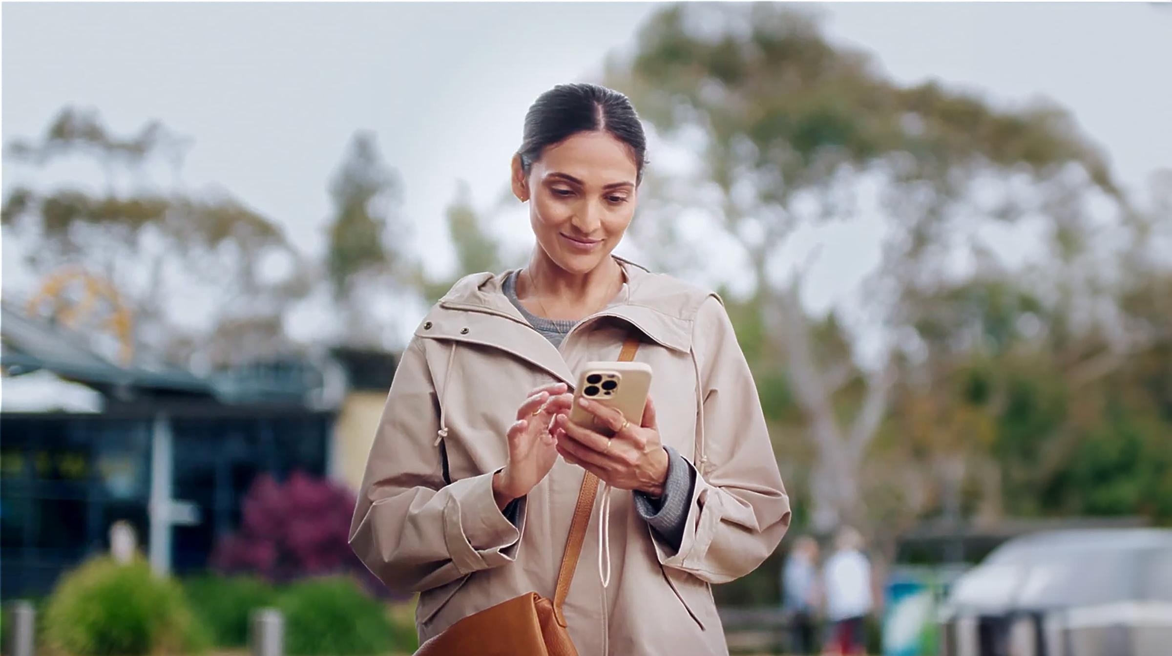 Smiling woman in a beige coat using a smartphone outside.