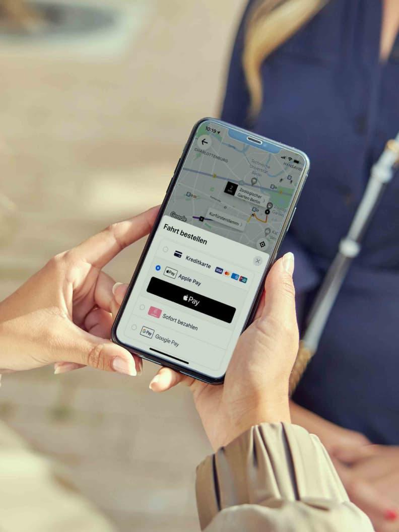 Close-up of hands holding a smartphone displaying a map and Adyen payment options including Apple Pay and Google Pay.