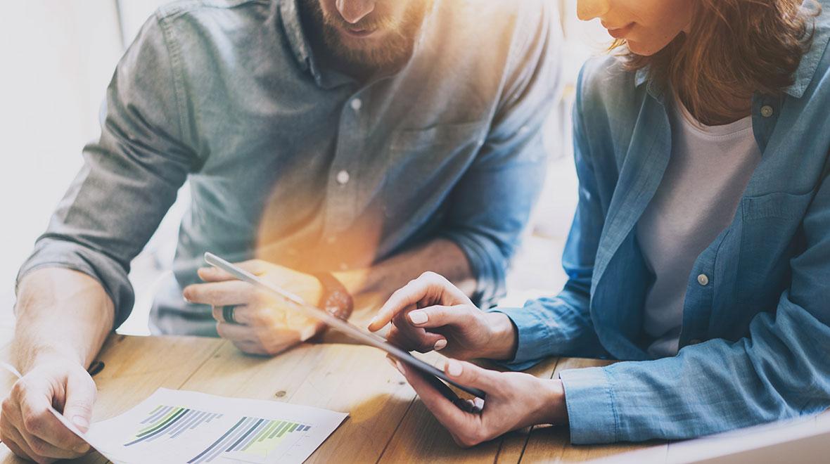 Dois profissionais colaborando em um tablet com gráficos de análise financeira em papel.