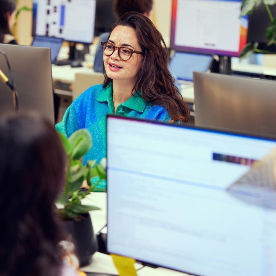 Smiling woman with glasses working at her desk in an office environment.