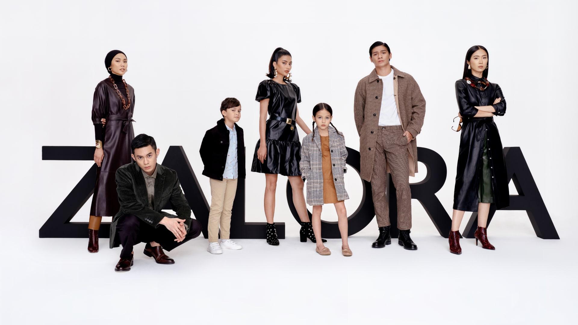 Seven diverse models posing in stylish outfits in front of large letters spelling ZALORA.