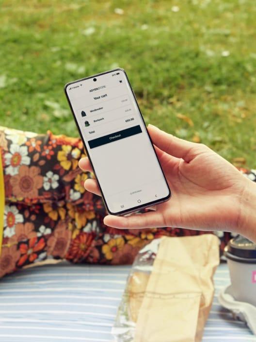 Osoba drží smartphone s viditelným obrazovkou Adyen checkout venku.