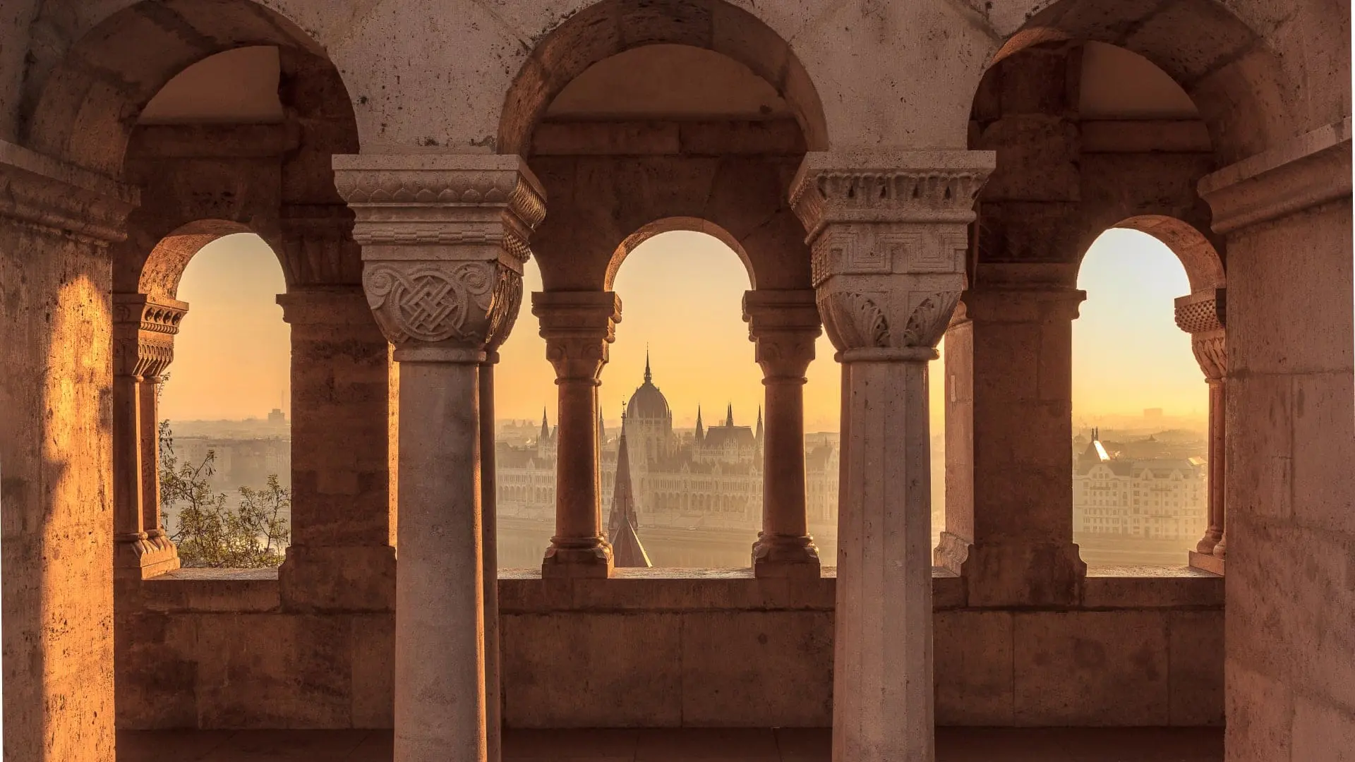 Sunrise view of the Hungarian Parliament Building through an archway.