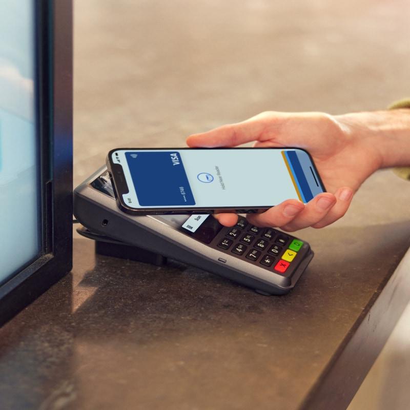 Persona que utiliza un smartphone para realizar un pago sin contacto en un lector de tarjetas.