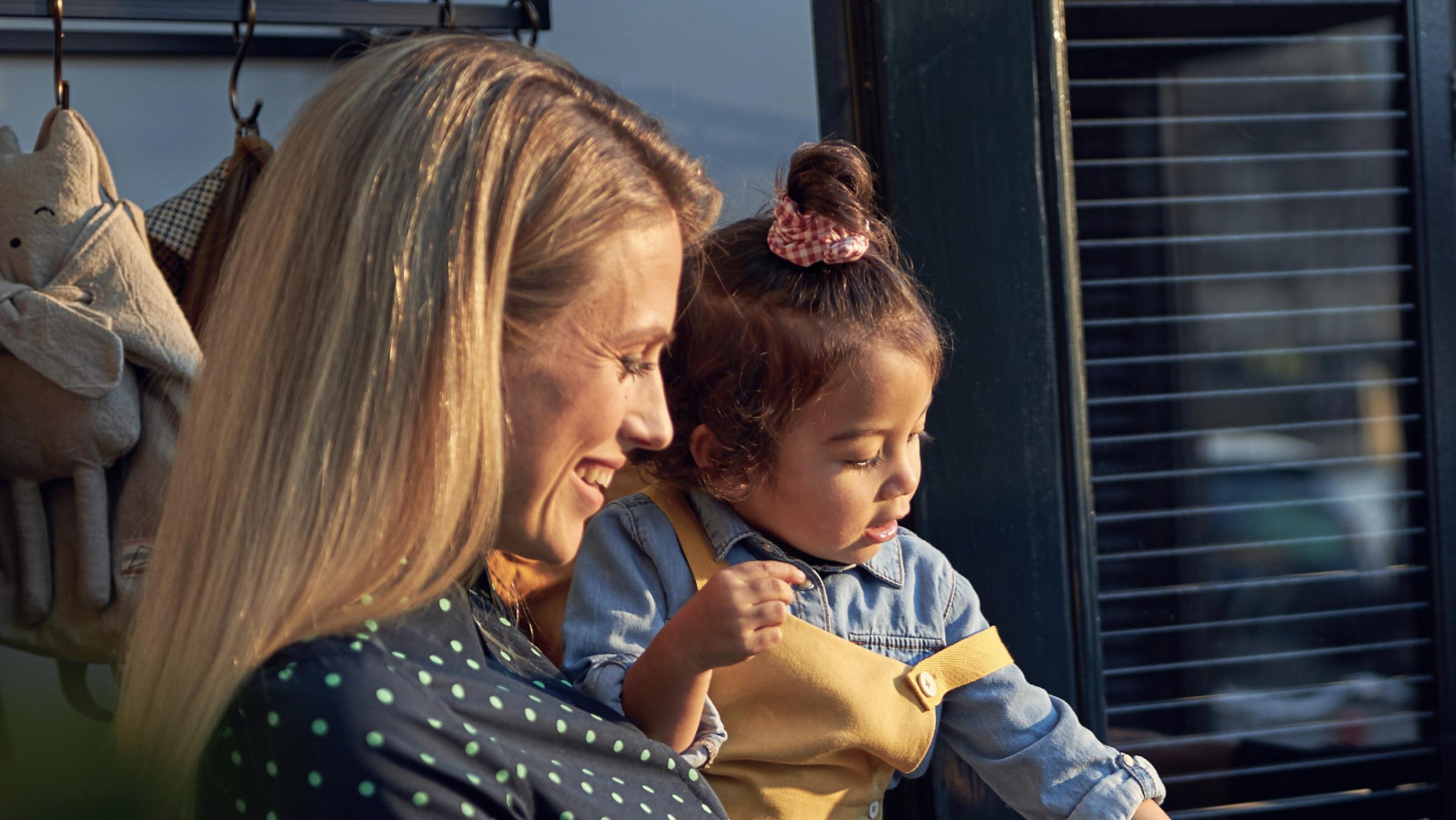 A smiling woman holding a young child who is looking away.